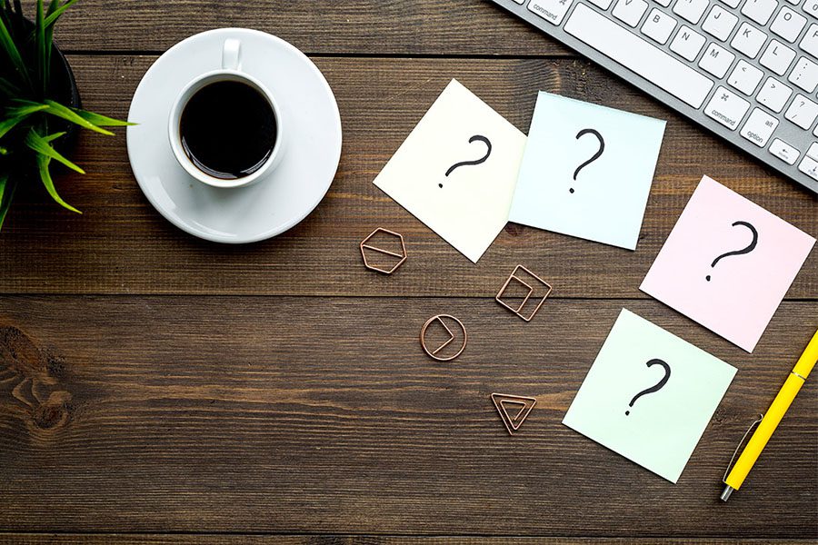 FAQ-Over-Head-View-of-Sticky-Notes-With-Question-Marks-on-a-Dark-Wooden-Computer-Desk-With-a-Cup-of-Coffee-and-a-Keyboard